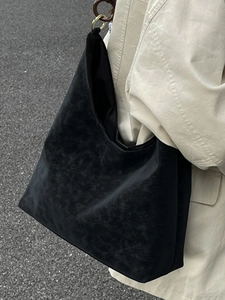 Large black minimalist tote bag with golden hardware shown on shoulder of a model