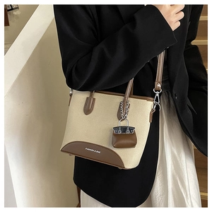 Detail of canvas bucket bag with brown leather trim and mini purse charm on a model