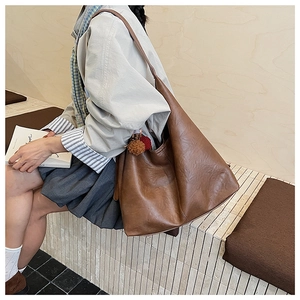 Detail showing brown large-capacity bucket bag with bi-color plush ball pendant on a model