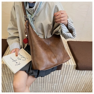 Detail of dark brown leather bucket bag with red plush charm on a shoulder strap