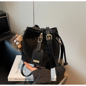 Detail of black suede bucket bag with gold hardware and brown plush monster charm