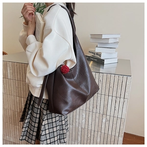 Detail of coffee brown large capacity bucket bag with cute red pompom on white sweatshirt