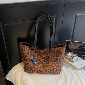 Détail du sac cabas en daim léopard avec anses en cuir sur un fond de literie blanc