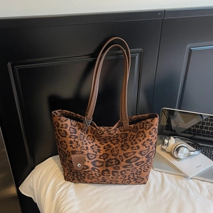 Détail d'un sac cabas léopard en daim avec des anses en cuir marron et un pendentif