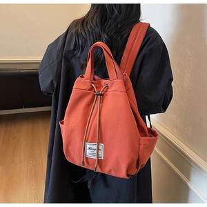 Close-up of brick red canvas drawstring backpack with adjustable straps and woven label