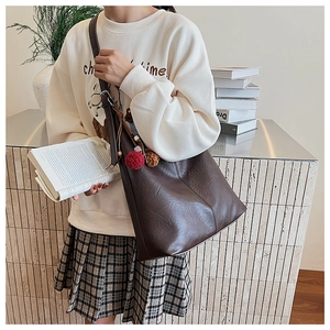 Detail view of deep brown large tote bag with pleated texture and pompom charm decoration