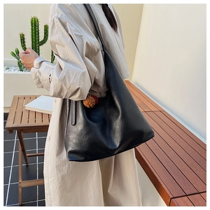 Detail of black large capacity leather bucket bag with a trendy red fur pompom charm