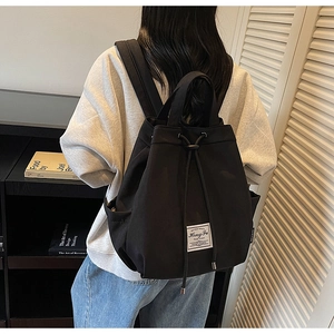 Detail of minimalist black canvas backpack featuring drawstring closure and white logo patch