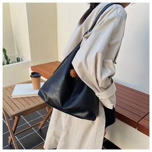 Detail of a large black leather bucket bag with a brown fuzzy charm on shoulder strap