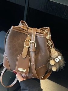 Deep brown bucket bag with plush monster charm and smooth synthetic leather details