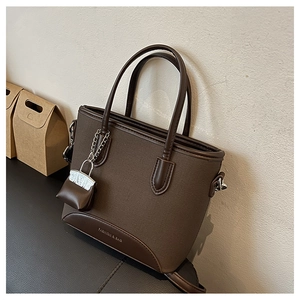 Detail of dark brown canvas and leather bucket bag with silver chain and mini pouch charm