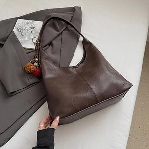 Detail view of large dark brown leather bucket bag with folk-style plush charm and accessories