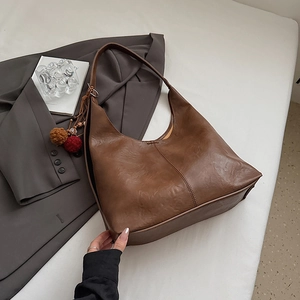 Detail of dark brown grained leather tote bag with stylish pompom and bead charm