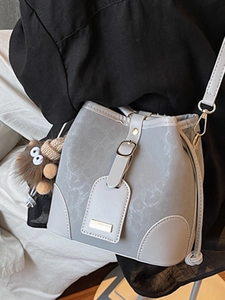 Light grey bucket bag with textured pattern and cute brown plush charm on fine strap