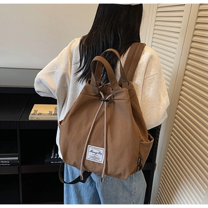 Detail view of the warm brown canvas backpack showing drawstring closure and side pockets