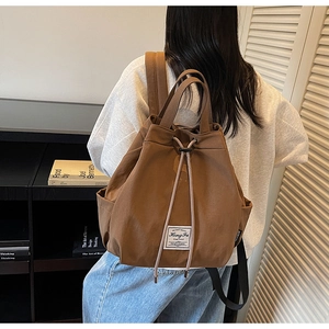 Brown canvas drawstring backpack with top handle and side pockets shown in a lifestyle setting