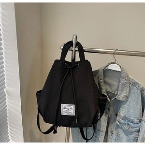 Detail of black drawstring canvas backpack featuring vintage patch on white wall