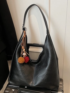 Fashionable black large capacity bucket bag with decorative tassel on a white door