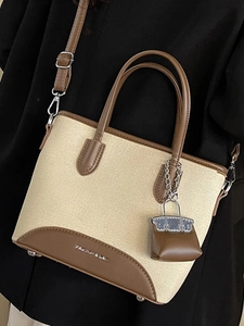 Chic beige canvas and brown leather bucket bag with a mini charm and shoulder strap