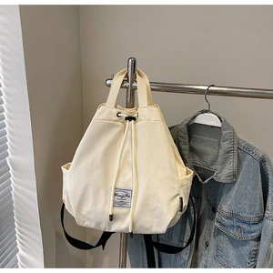 Detail of off-white canvas drawstring backpack with brand patch and black straps