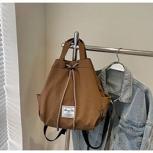 Brown canvas bucket backpack with drawstring closure and handle shown in a lifestyle scene