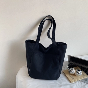 Close-up of black nylon tote bag showing the side white tag and front pocket detail