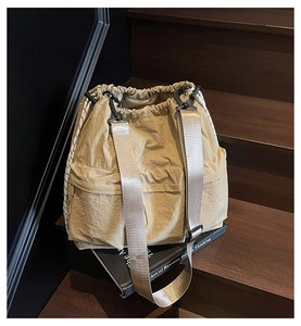 Detail view of khaki nylon bucket bag with adjustable straps and drawstring on wood steps