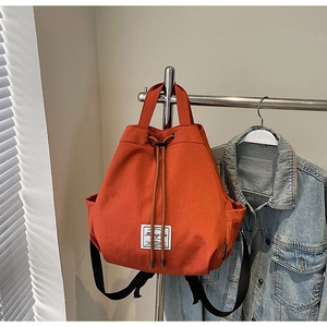 Detail view of the orange canvas backpack featuring drawstring closure and top handle strap