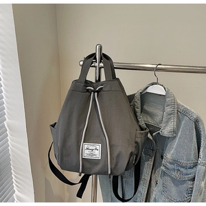 Detail view of a dark grey multifunctional drawstring backpack with woven label on a metal rack
