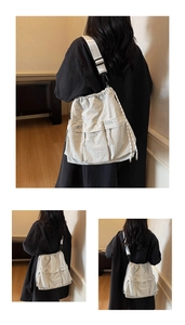 Detail of a beige nylon drawstring crossbody bag with multiple pockets and white strap