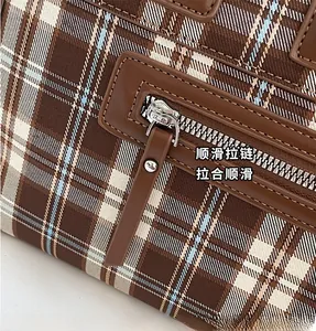 Detail view of the smooth silver zipper and brown leather trim on a plaid tote bag