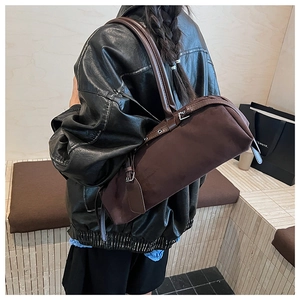 Detail view of a dark brown suede cylindrical shoulder bag worn by a model