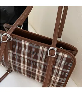 Detail of adjustable brown leather shoulder strap on a brown plaid tote bag