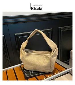 Détail d'un sac cabas en daim kaki avec large bandoulière posé sur un banc en bois