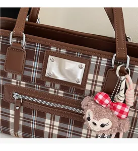 Detail of brown plaid tote bag featuring silver metal hardware and a plush charm detail