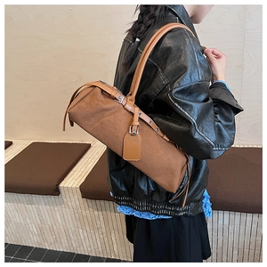 Close-up of a brown suede baguette bag with leather straps and metal buckles on a shoulder