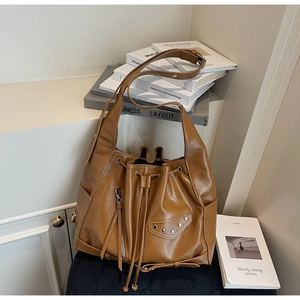 Detail view of brown bucket bag featuring metal rivets, side zipper and stylish tassels