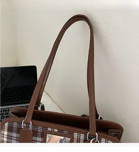 Detail of a brown plaid tote bag featuring leather handles and silver metal D-rings