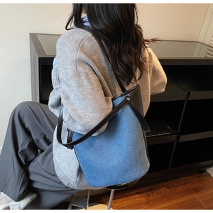 Detail view of denim bucket bag with black leather trim worn on the shoulder by model