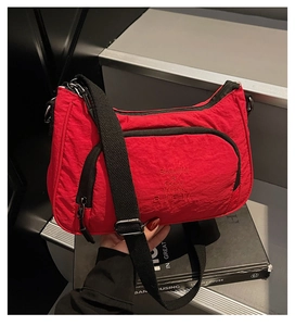 Detail of red textured nylon crossbody bag featuring black zipper and white embroidery