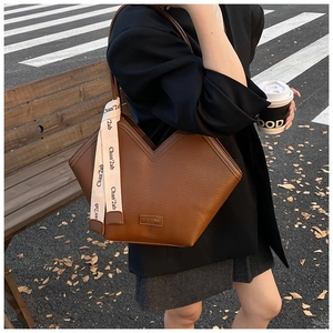 Detail of a brown leather tote bag featuring a V-shaped top and a silk scarf on the handle