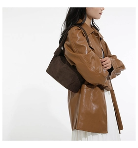 Sac à bandoulière en suédine marron porté avec une veste en cuir et jupe plissée
