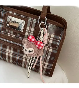 Detail view of a plush bear charm with a checkered bow hanging on a large brown tote bag