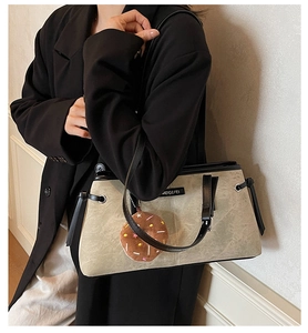 Dettaglio della borsa tote grigio-beige con bordo nero e ciondolo a forma di donut