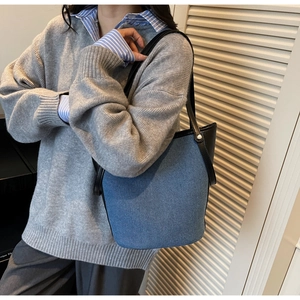 Detail of blue denim textured bucket bag with black leather straps on a casual model outfit