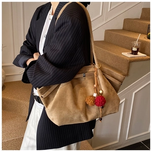 Gros plan d'un sac cabas en daim marron avec boucle métallique et pompon doux