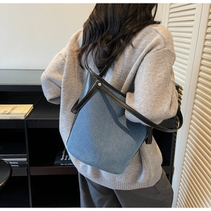 Detail view of denim bucket bag with black leather trim and silver rivets on a model