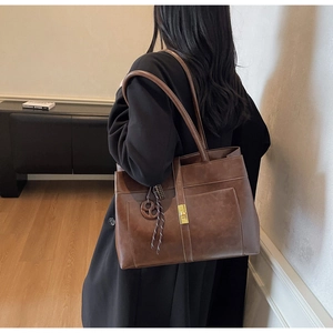 Détail d'un sac cabas rétro marron avec boucle dorée et breloque en cordon tressé