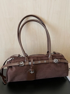 Retro dark brown suede boston bag with multiple belt straps on a warm wood background