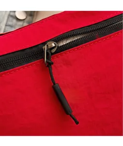 Detail of red nylon shoulder bag featuring a black zipper with long knotted cord pulls